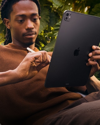 A person outside by foliage holding their iPad Pro in one hand and Apple Pencil Pro in the other